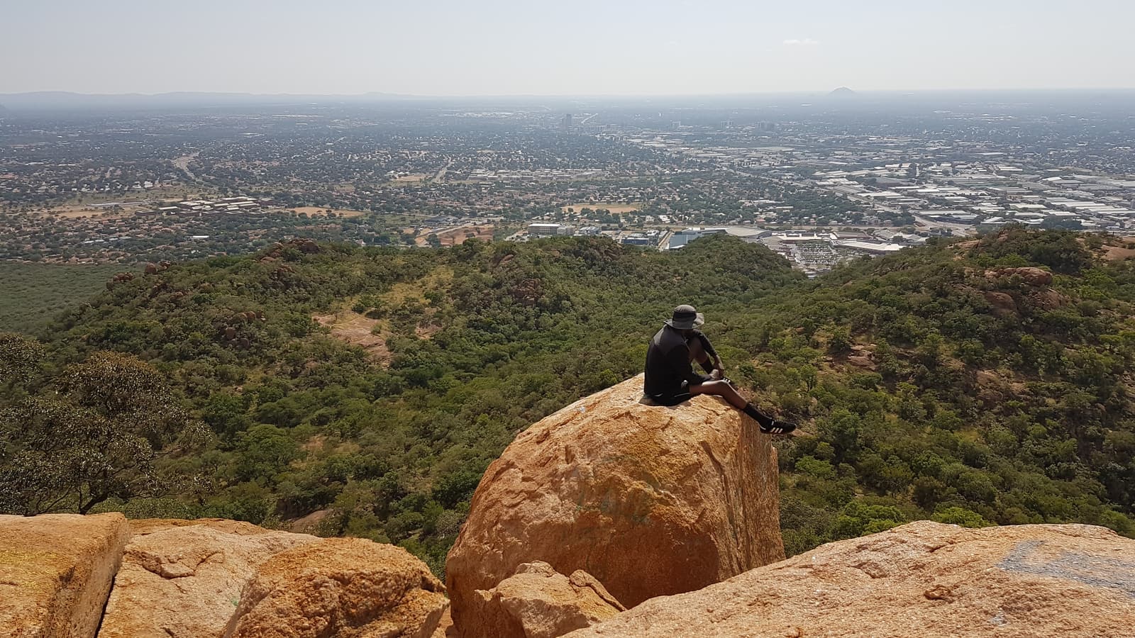 A hiker on a boulder at the summit of Kgale Hill looking over Gaborone